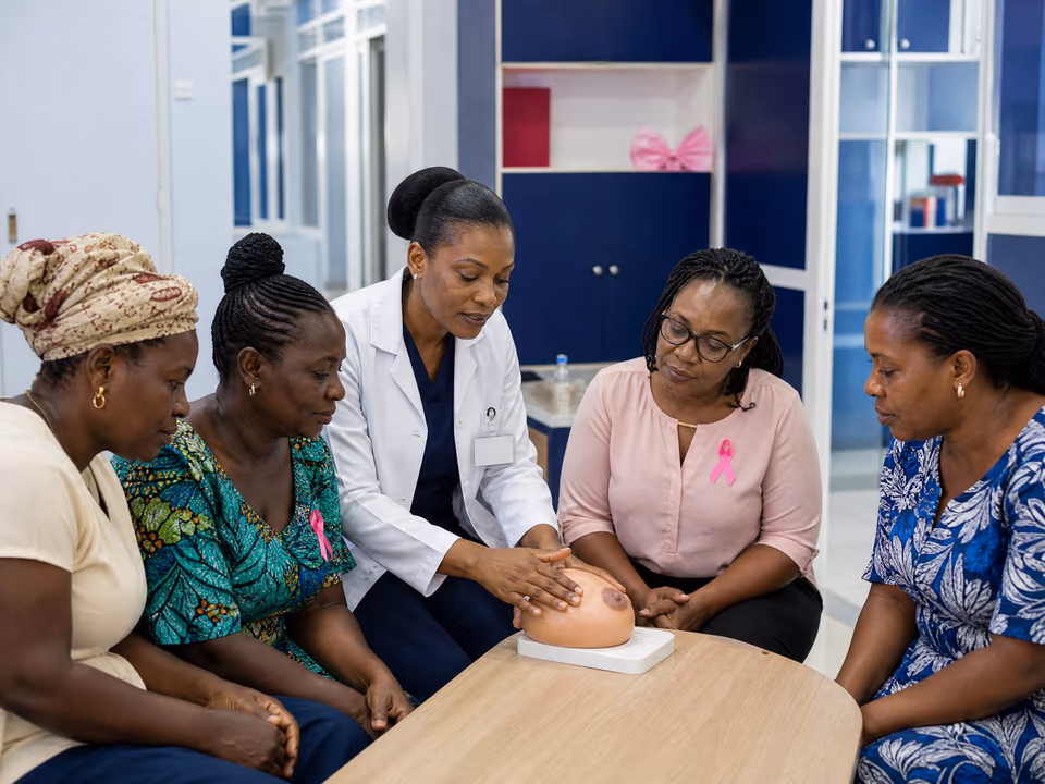 Illustrative scene: A doctor in a white coat shows four women how to examine the breast on a silicone model at a round table.