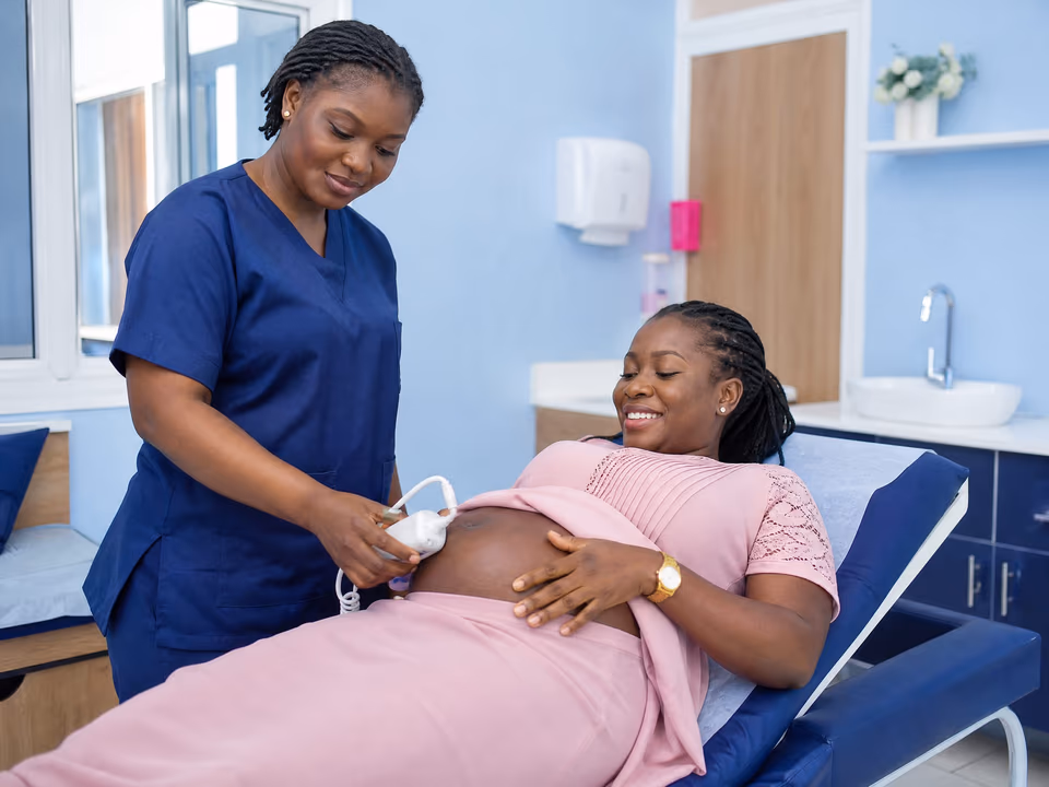 Illustrative scene: A midwife listens to the baby's heartbeat with a handheld doppler on the belly of a smiling pregnant woman.