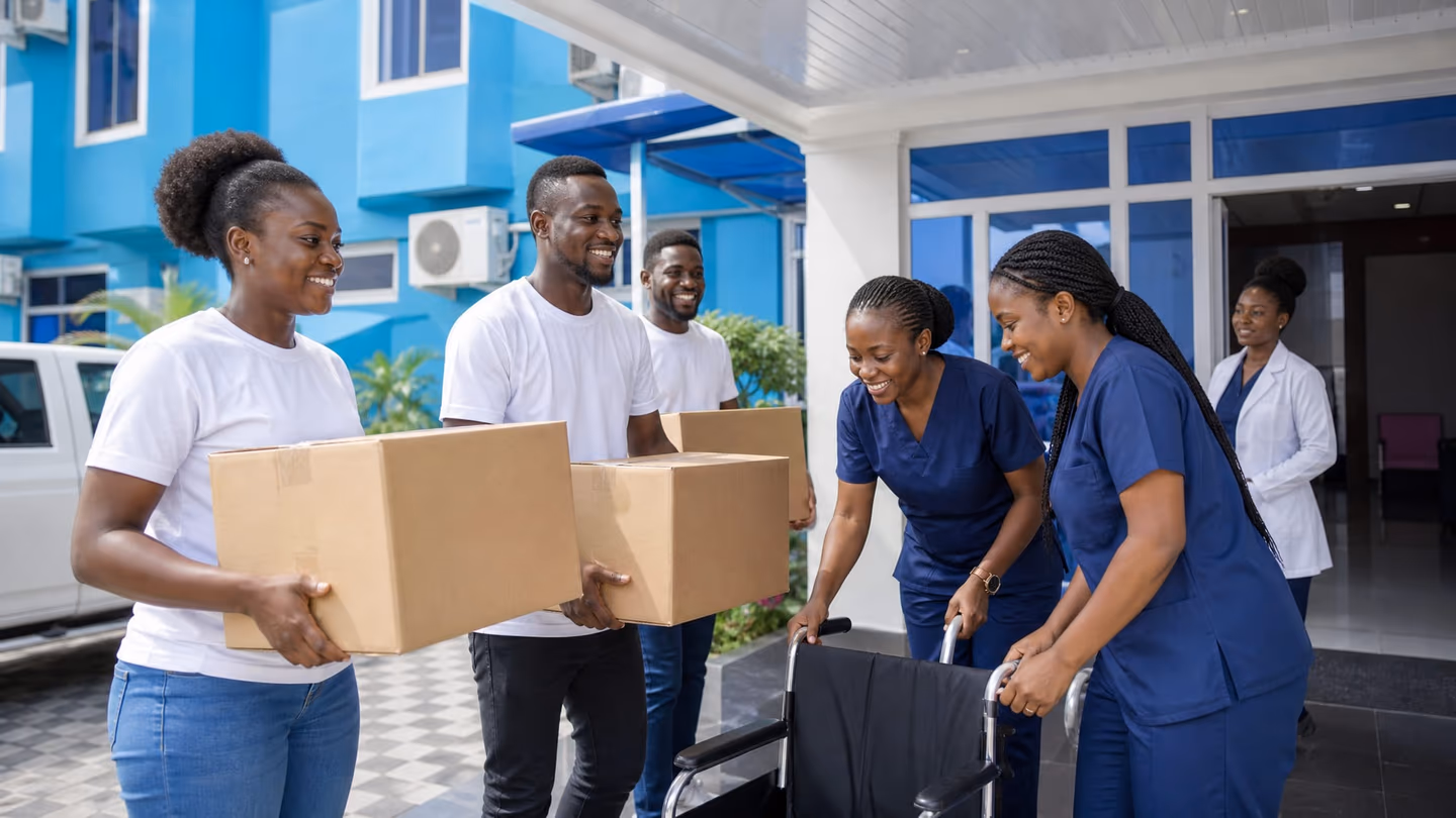 Illustrative scene: Volunteers in white T-shirts carry boxes and nurses wheel in a new wheelchair at the hospital entrance.