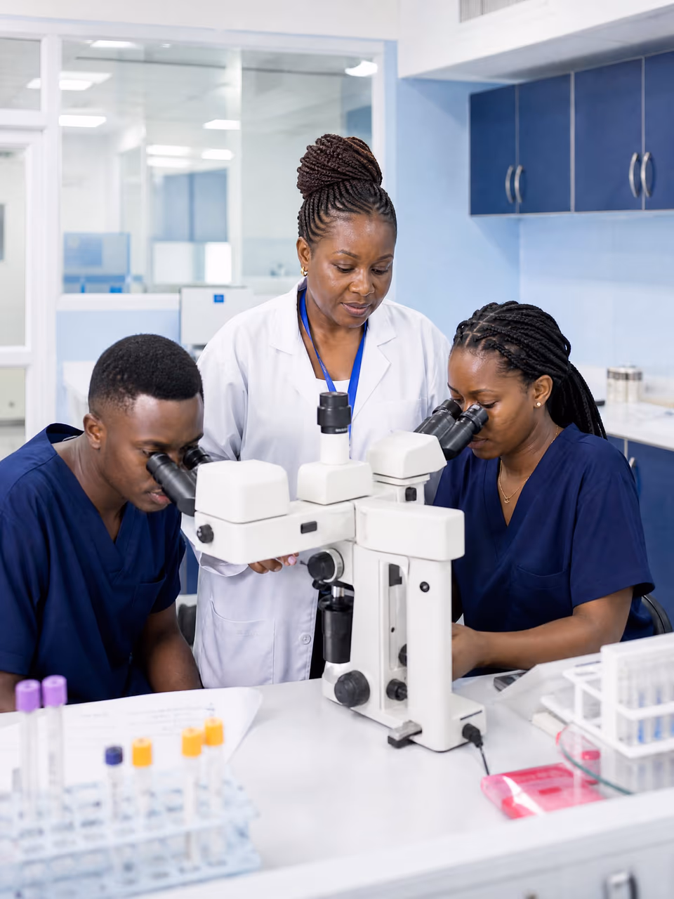 Illustrative scene: A senior clinician watches two junior doctors look through a teaching microscope in a laboratory.